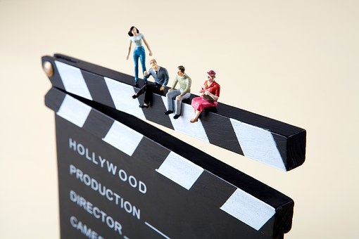 Das Foto zeigt eine Filmklappe, auf der Miniaturmenschen (Puppen) sitzen, Quelle: Pixabay