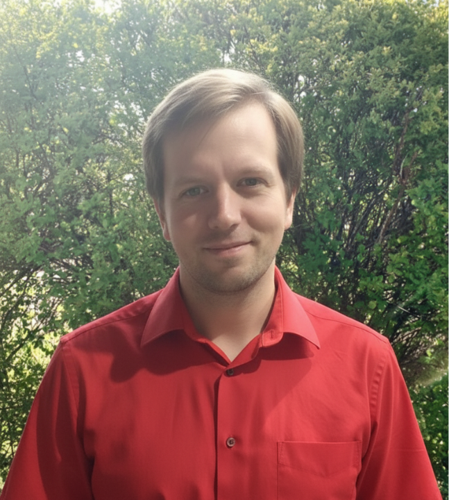 Der Berater Felix Reischmann steht, schaut freundlich und hat ein rotes Hemd an