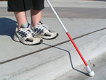 Abbildung: Eine blinde Frau ertastet den Straßenrand mit einem Blindenstock