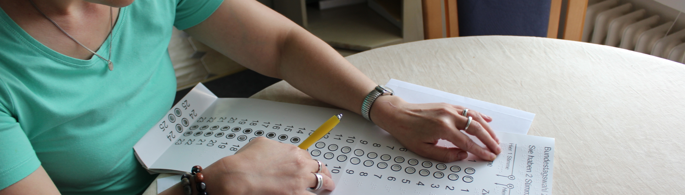 Eine Frau liest die Brailleschrift auf einer Wahlschablone Eine Frau liest die Brailleschrift auf einer Wahlschablone