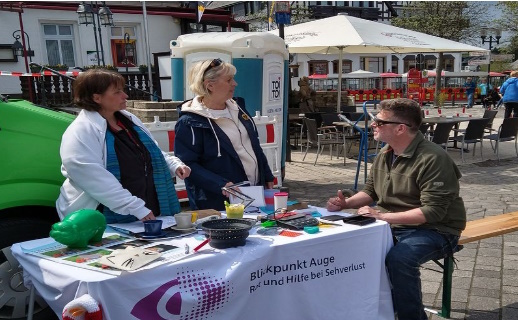 Zwei frauen und ein mann umringen den stand von blickpunkt auge auf einem platz